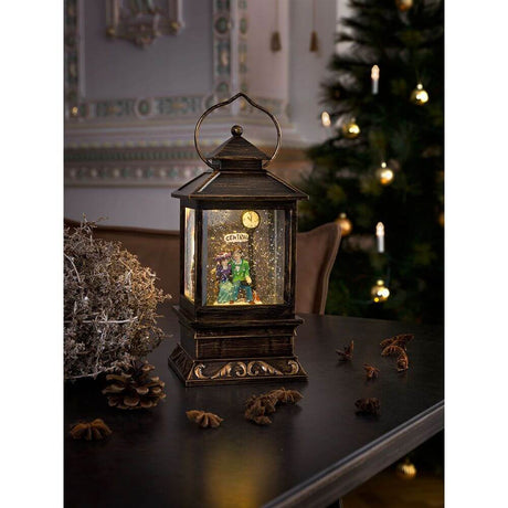 LED Schneelaterne mit Pärchen klein Timer wassergefüllt batteriebetrieben auf einem Tisch mit Tannenzapfen und Weihnachtsbaum im Hintergrund.