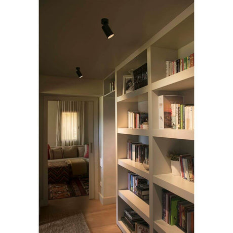 LED Wandstrahler STAN 12W 2700K Schwarz an Decke über Bücherregal in modernem Raum.