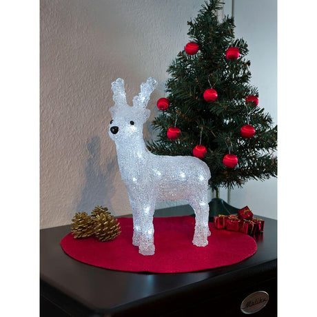 LED Acryl Rentier 24 Kaltweiße Dioden batteriebetrieben vor dekorativem Weihnachtsbaum.