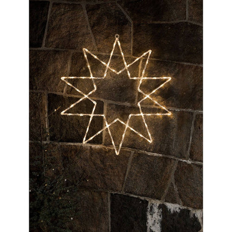 LED Acryl Stern 10 Zacken 120 Warmweiße Dioden IP44 beleuchtet an einer Steinmauer.