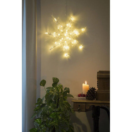 LED Grande étoile en acrylique 32 diodes blanc chaud éclairée dans une pièce chaleureuse avec bougie et plante.