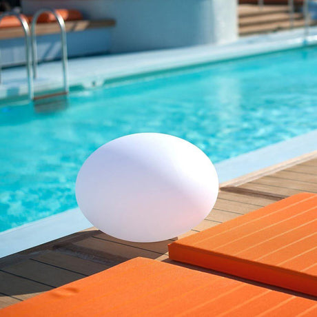 LED Lampada a batteria Flatball L con controllo tramite app accanto a una piscina su lettini prendisole.