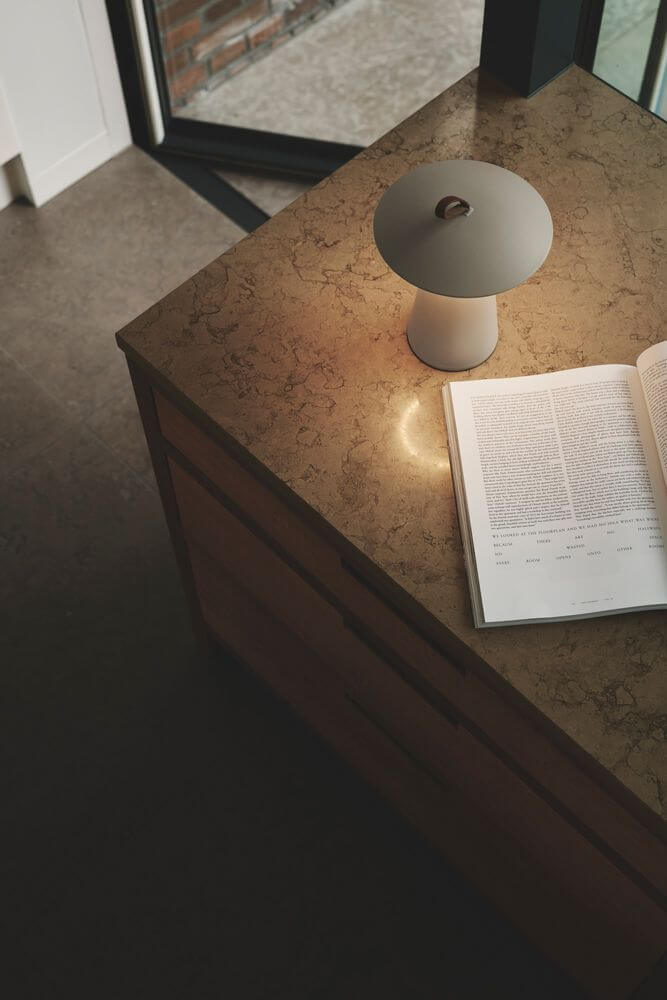 LED Akkuleuchte Ara To-Go 2 IP54 auf einem Tisch mit Buch und sanftem Licht in einem modernen Raum.