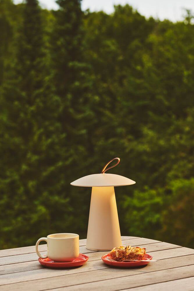 LED Akkuleuchte Ara To-Go 2 IP54 auf einem Tisch mit einer Tasse und Gebäck im Freien.