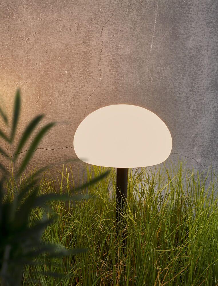 LED Akkuleuchte Sponge Spike IP65 in elegantem, pilzförmigem Design im Gras vor einer Betonwand.