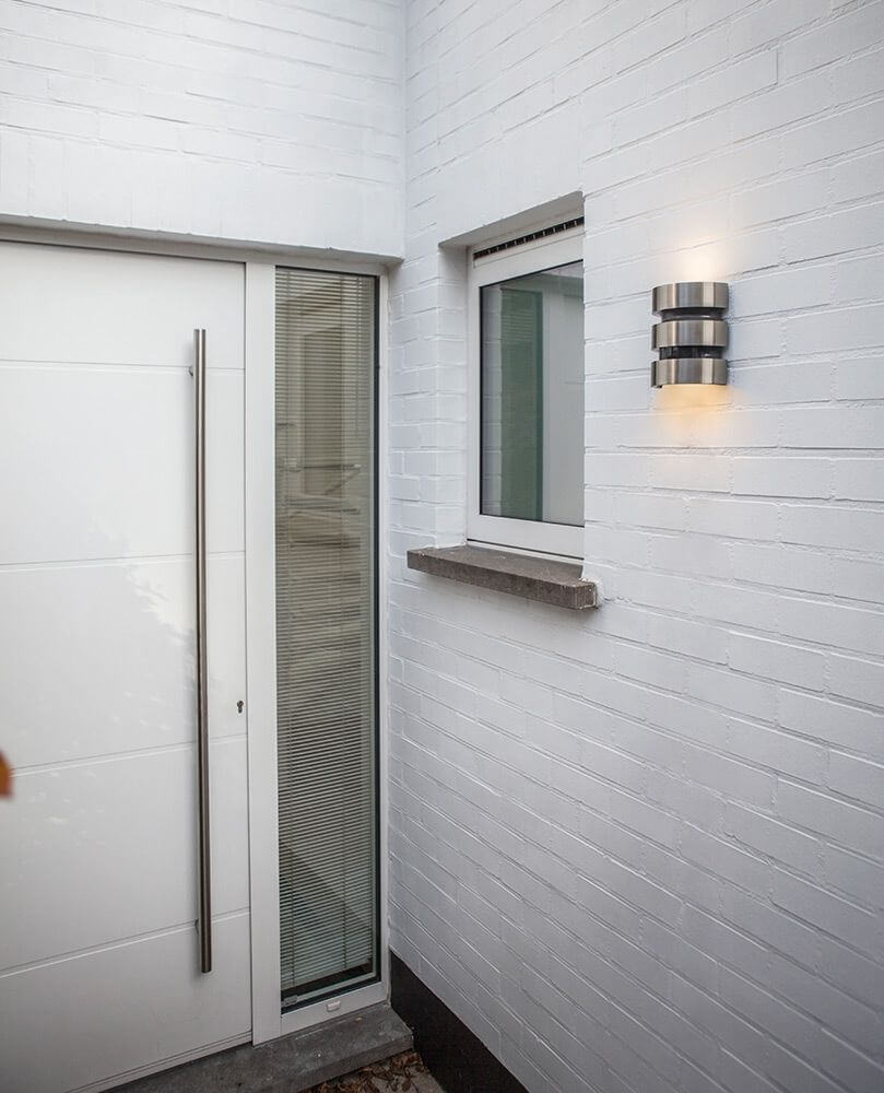 LED Außenleuchte Maya IP44 Edelstahl mit Bewegungsmelder an einer weißen Wand neben der Eingangstür.