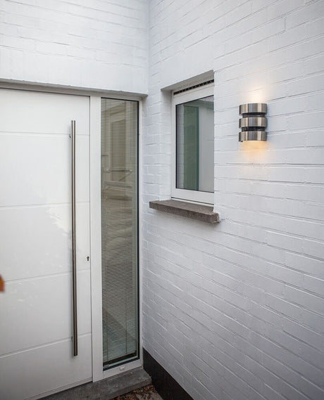 LED Außenleuchte Maya IP44 Edelstahl mit Bewegungsmelder an einer weißen Wand neben der Eingangstür.