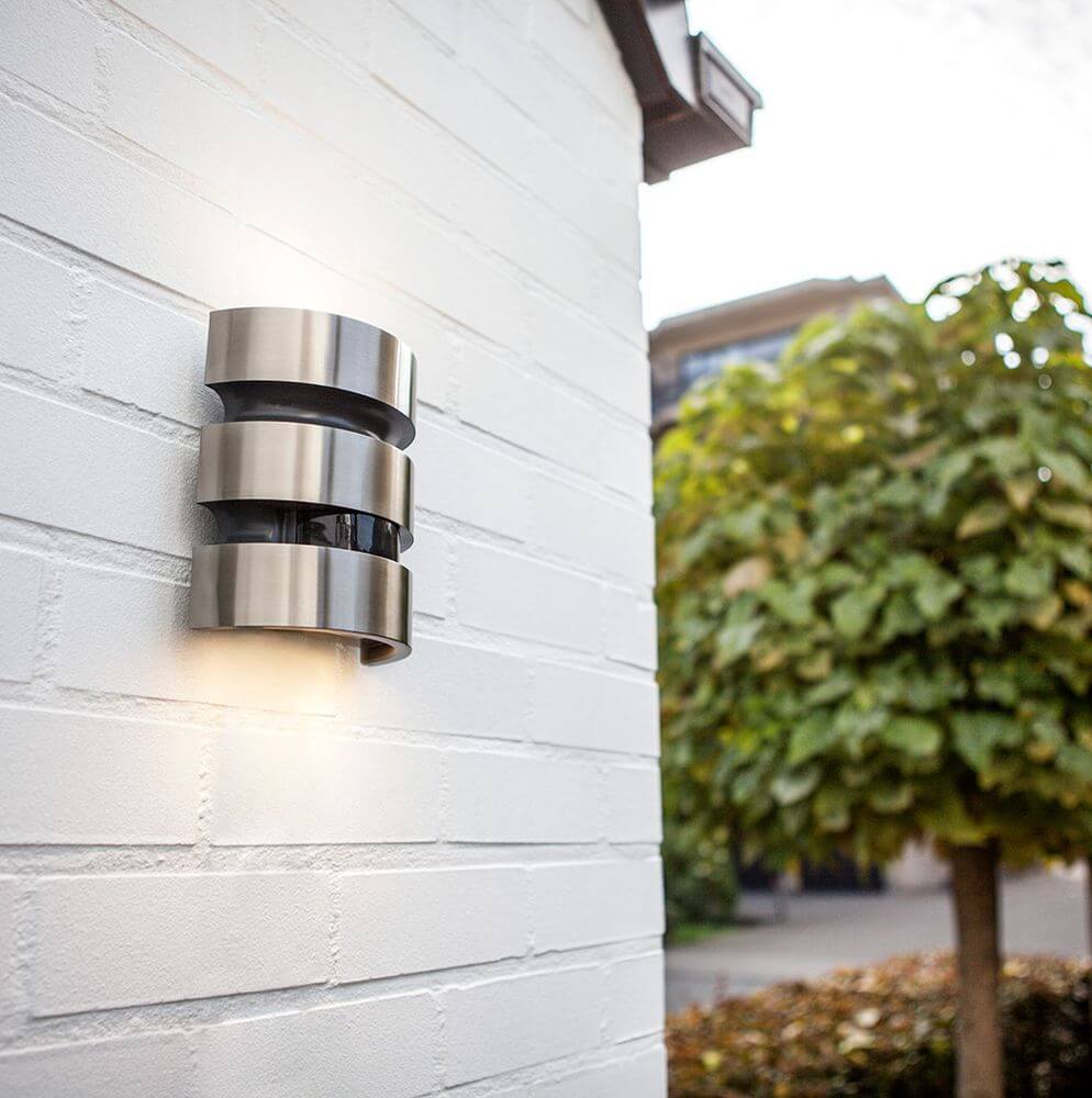 LED Außenleuchte Maya IP44 Edelstahl mit Bewegungsmelder an einer Wand installiert, strahlt modernes Licht aus.