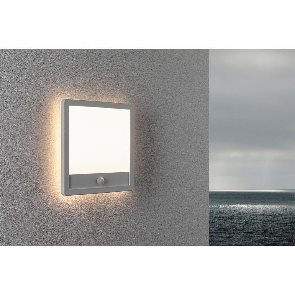 LED Außen Wandleuchte Lamina Bewegungssensor Weiß an einer Wand mit sanftem Licht und Meer im Hintergrund.