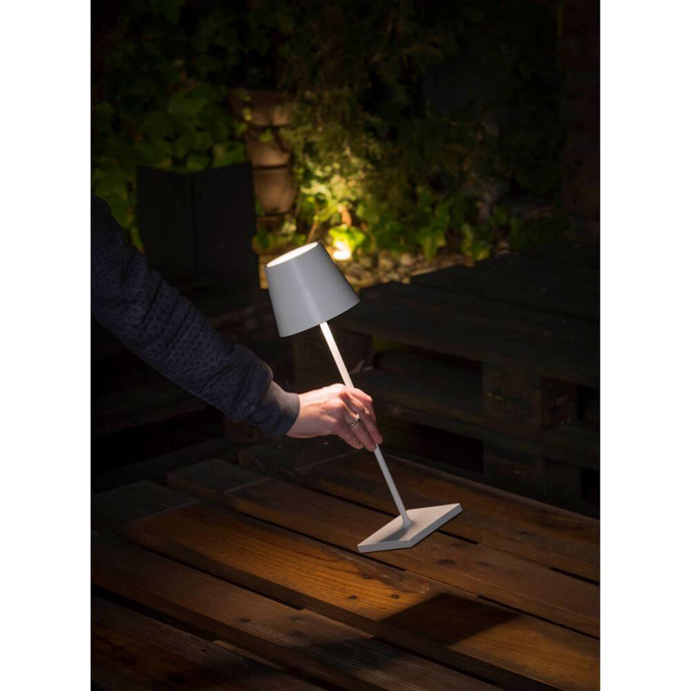 LED Akku-Außentischlampe TOC IP54 Weiß auf einem Holztisch im Freien bei Nacht.