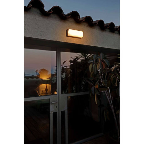 LED Außenwandlampe HALF 3000K IP65 Schwarz an einer Wand mit warmem Licht in der Dämmerung.