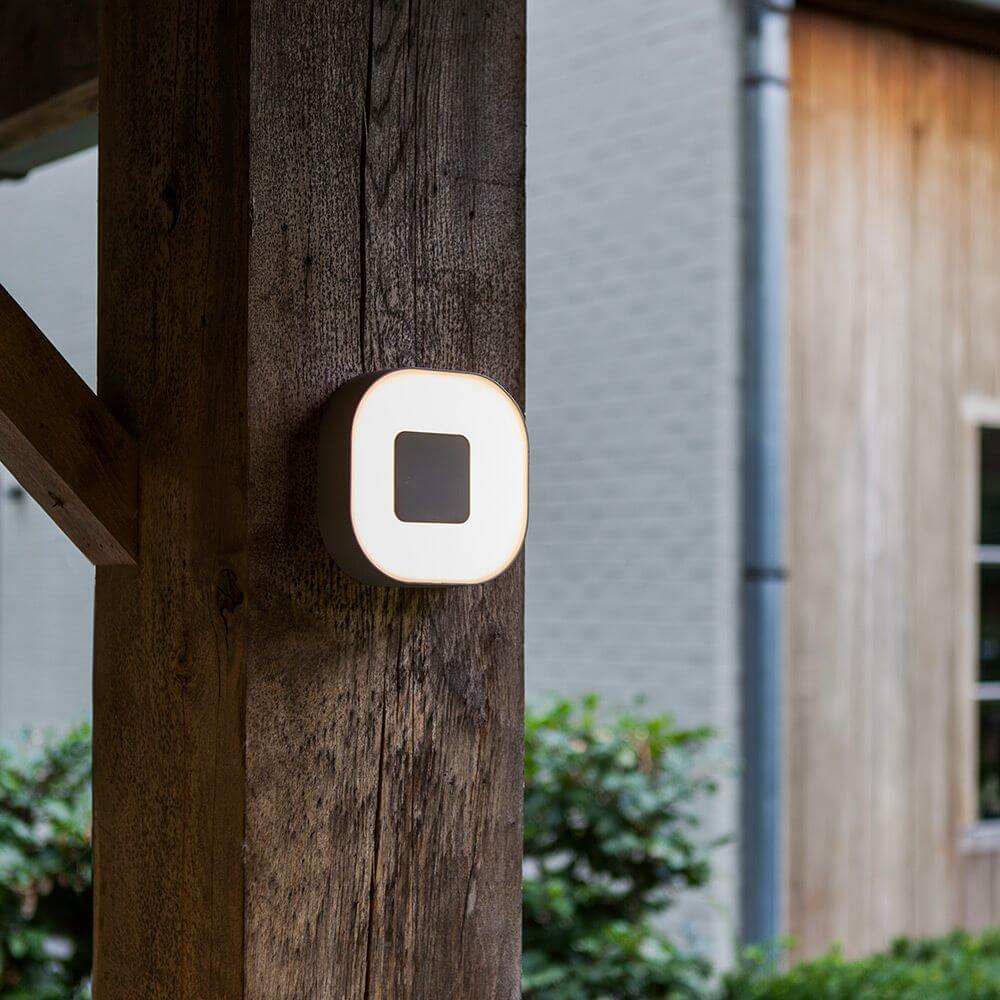 LED Außenwandlampe Ublo 16x16cm IP44 Grau an Holzpfeiler montiert im Außenbereich.