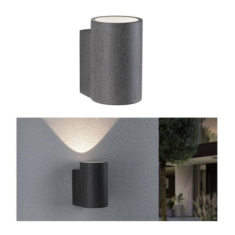 Beton LED Concrea udendørs væglampe sandsort IP65 på en væg udsender varmt lys for stilfulde accenter.