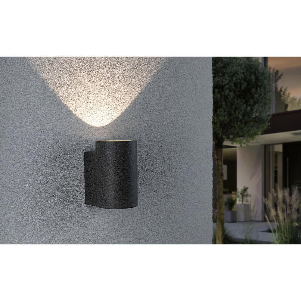 Beton LED Außenwandleuchte Concrea Sandig-Schwarz IP65 an einer Wand montiert, strahlt warmes Licht aus.