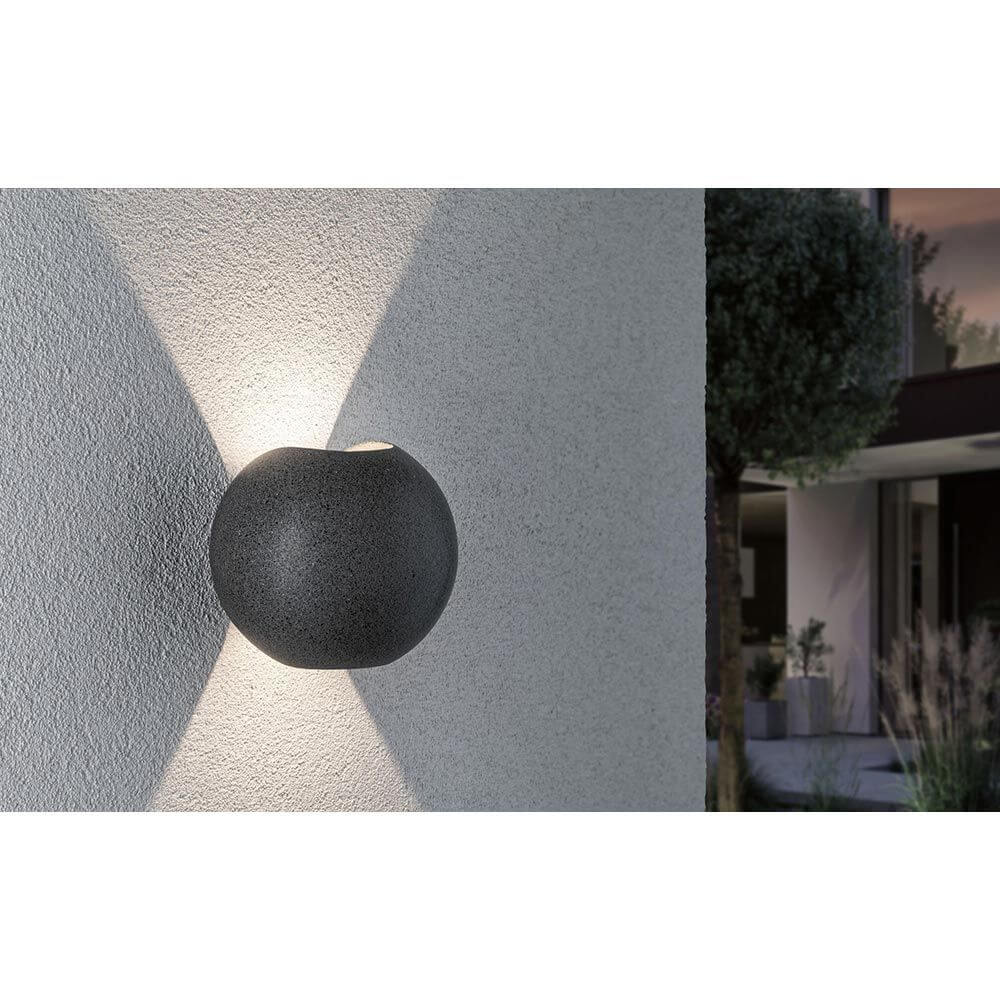LED Außen Wandleuchte Concrea Schwarzer Sandstein Beton IP65 an einer Wand montiert, strahlt elegantes Licht aus.