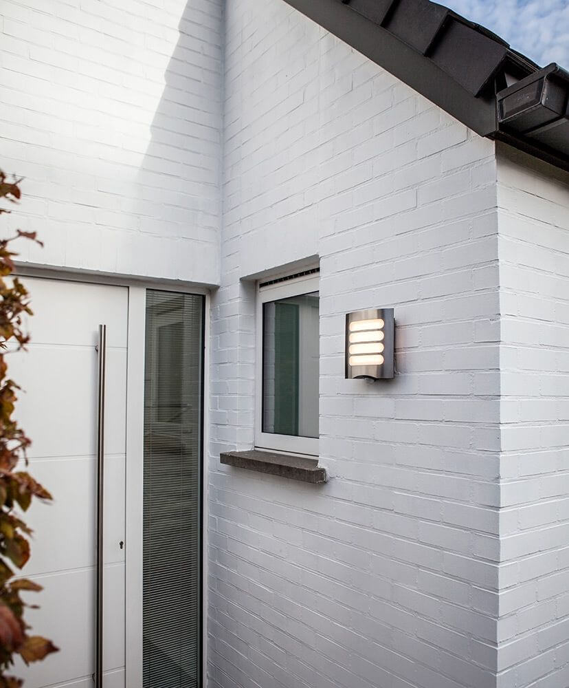 LED Außenwandleuchte Farell mit Sensor IP44 Edelstahl an einer weißen Hauswand montiert.
