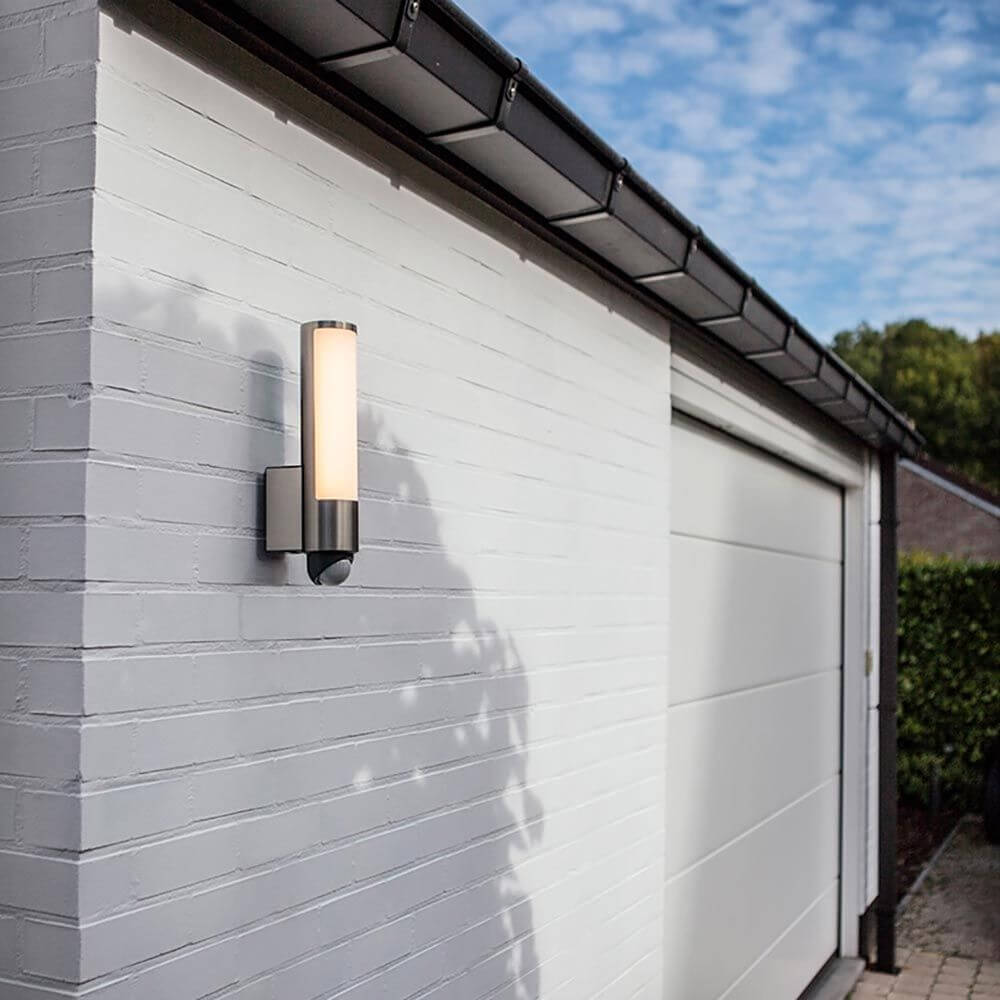 LED Außenwandleuchte Leda mit Sensor IP44 Edelstahl an einer weißen Wand montiert, beleuchtet die Umgebung.