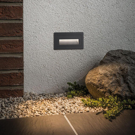 LED Outdoor wall recessed light Long Black IP65 on an exterior wall, surrounded by stones and gravel.