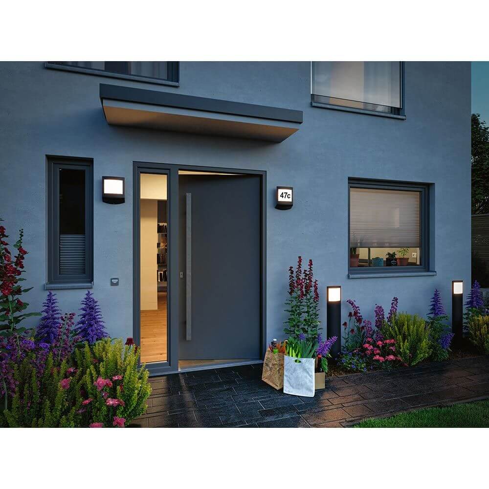 Moderne LED Hausnummernleuchte Padea an einer Wohnwand mit Dämmerungssensor und attraktivem Garten.