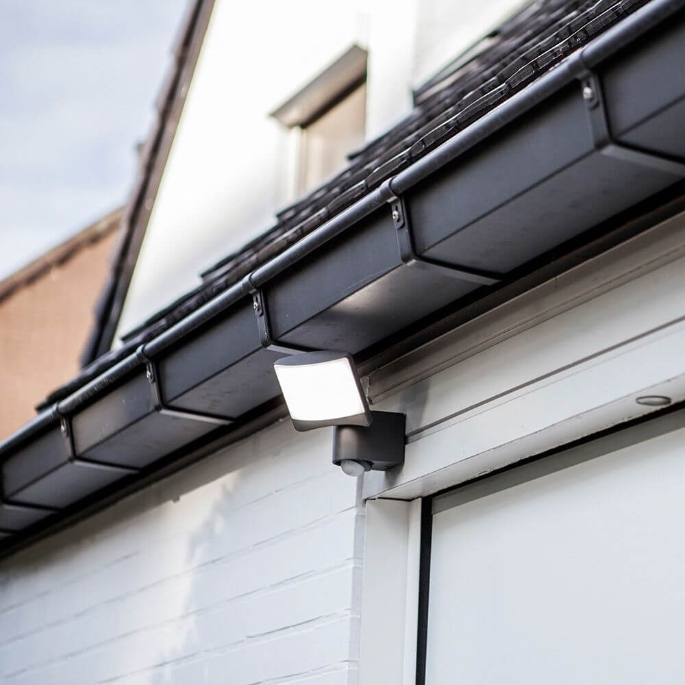 LED Außenstrahler Sunshine mit Sensor IP44 Anthrazit an einer Hauswand montiert, strahlend gleichmäßiges Licht.