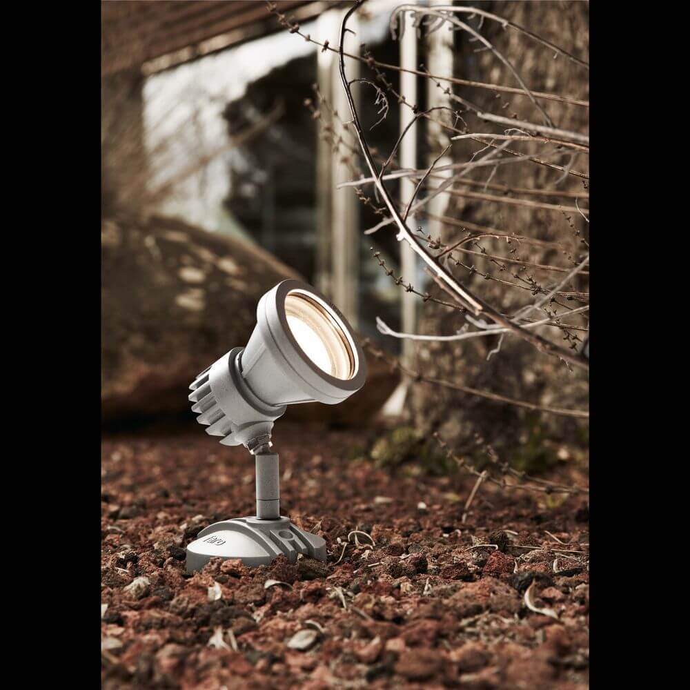 LED Außenwandstrahler MINIPROJECT IP65 Grau im Garten auf brauner Erde installiert.