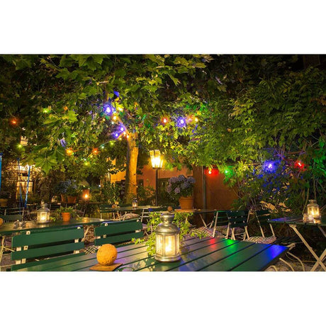 LED Biergartenkette 20er bunt milchig 160 Warmweiße Dioden 24V beleuchtet einen Garten mit Tischen und Laternen.