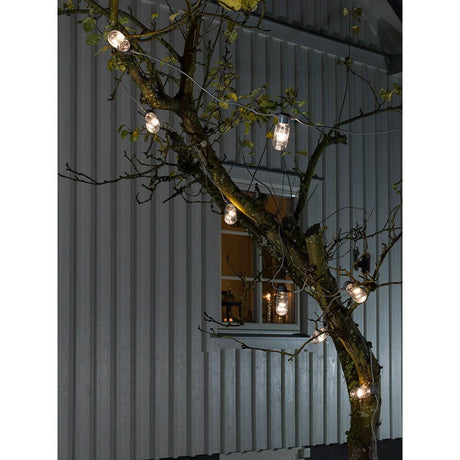 LED 10er-Biergartenkette klar Warmweiß 24V an einem Baum befestigt, strahlend in der Nacht.