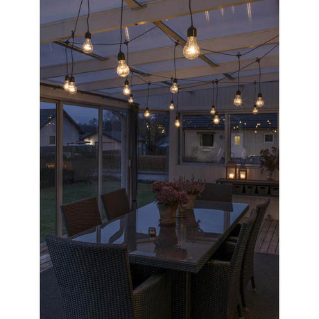 LED Lichtervorhang 20 klare Birnen 160 bernsteinfarbene Dioden IP44 in einem beleuchteten Gartenbereich.