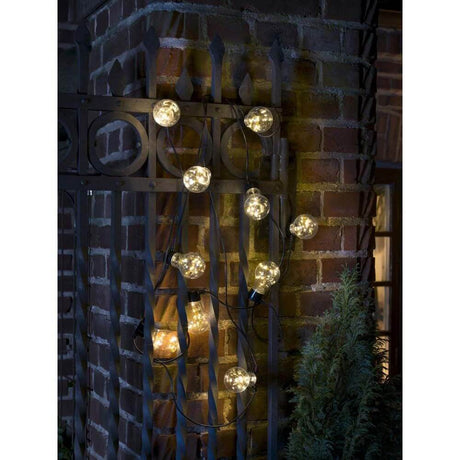 LED Biergartenkette mit 10 klare Birnen Bernstein IP44 um eine Gartenmauer hängend, stimmungsvolles Licht.