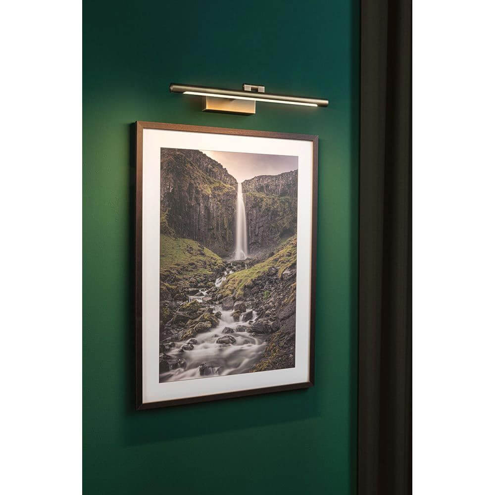 Moderne LED Bilderleuchte Mingo in Altmessing über einem gerahmten Landschaftsbild angebracht.