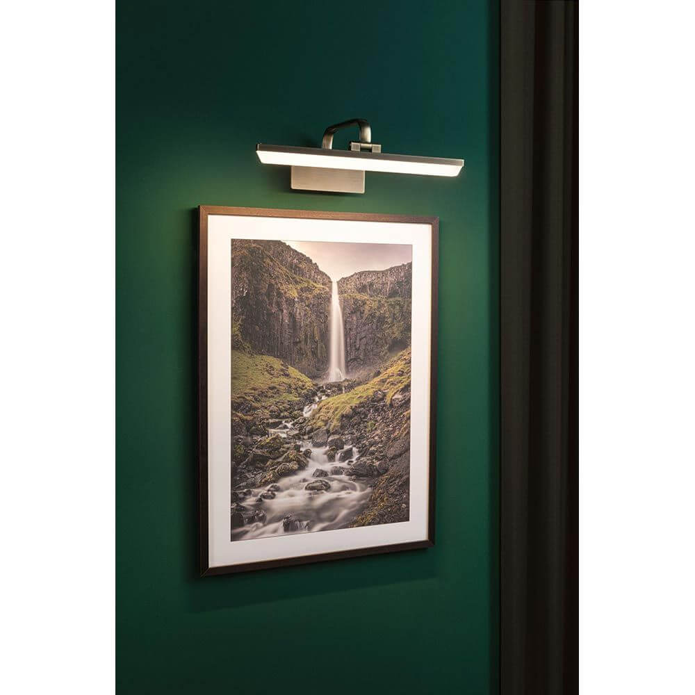 LED Bilderleuchte Renan Alt-Messing beleuchtet ein Kunstwerk an einer grünen Wand.