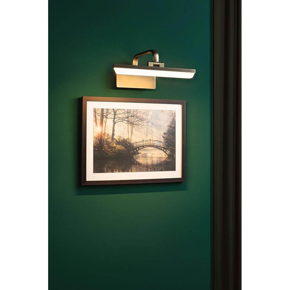 LED Spiegel-& Bilderleuchte Renan Messing-Antik beleuchtet ein Kunstwerk an der Wand.