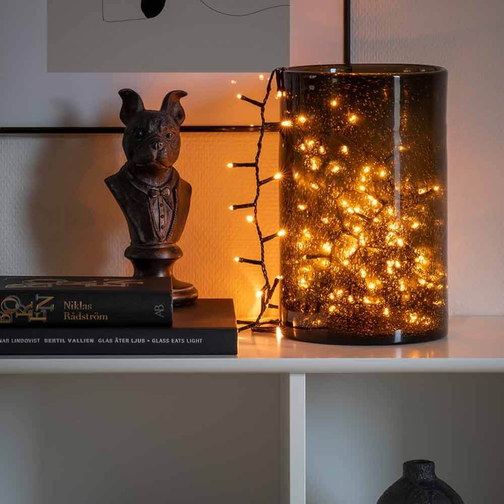 LED Büschellichterkette Cluster Schwarz in einem dekorativen Glasbehälter mit warmweißem Licht.