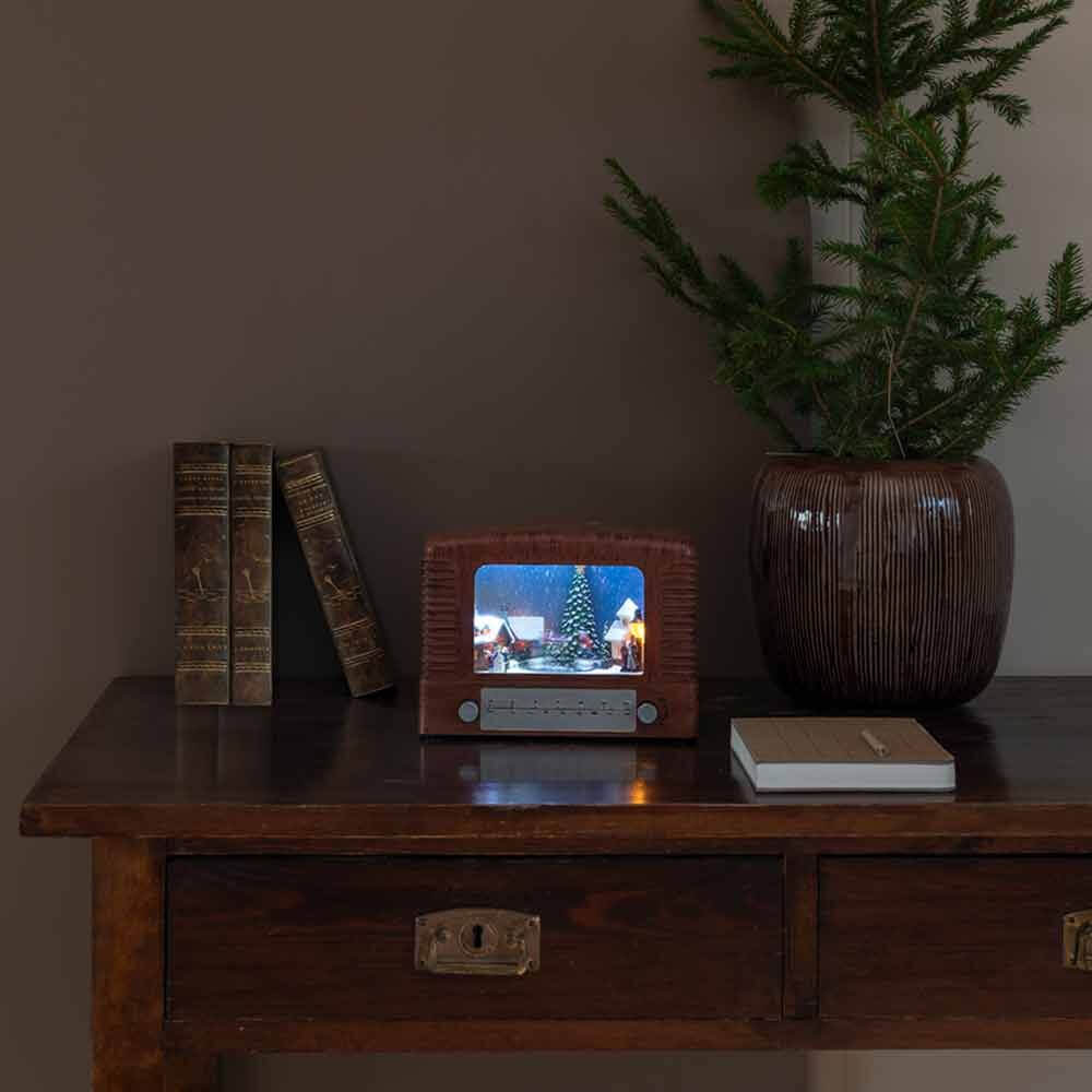 LED Dekoleuchte Radio mit Weihnachtsbaum, batteriebetrieben, auf einem Tisch mit Bücher und Pflanze.