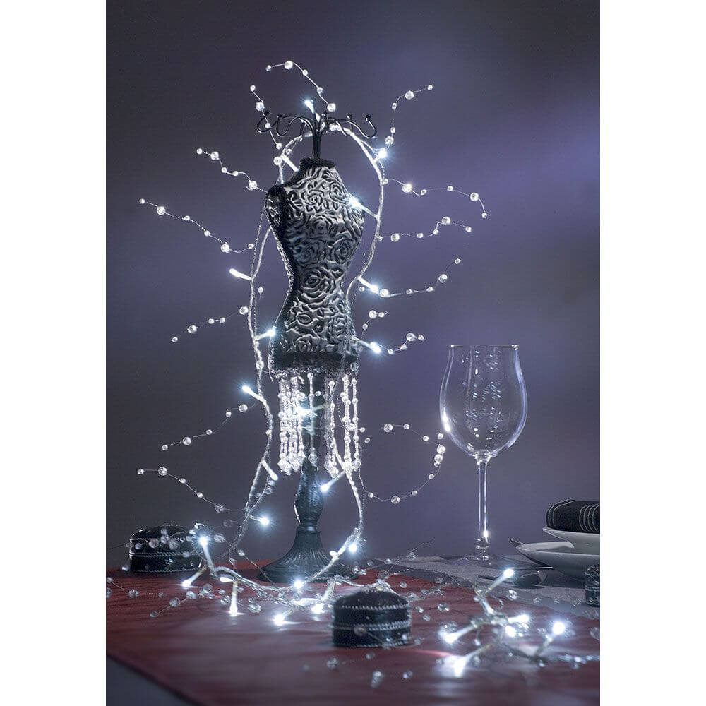 LED Dekolichterkette Acryl Perlen 32 Kaltweiße Dioden um eine elegante Statue mit Gläsern und dekorativen Elementen.