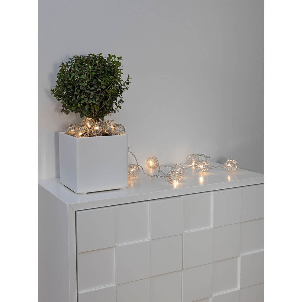 LED Dekolichterkette Aluminium-Drahtkugeln klein 16 Warmweiße Dioden batteriebetrieben auf einem Sideboard mit Pflanze.