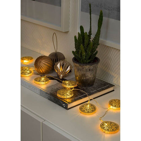 LED Dekolichterkette goldfarbene Metalltaler 10 Warmweiße Dioden batteriebetrieben auf einem Tisch mit Dekoration.