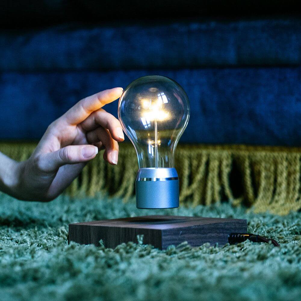 LED-Dekotischleuchte schwebende Glühbirne in einem stilvollen Wohnambiente mit Hand, die die Glühbirne berührt.