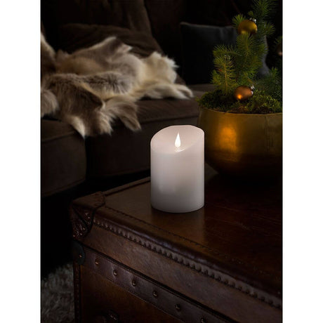 LED-ekte vokslys hvit med 3D-flamme 14 cm timer varmhvit batteridrevet på et bord ved siden av en plante.