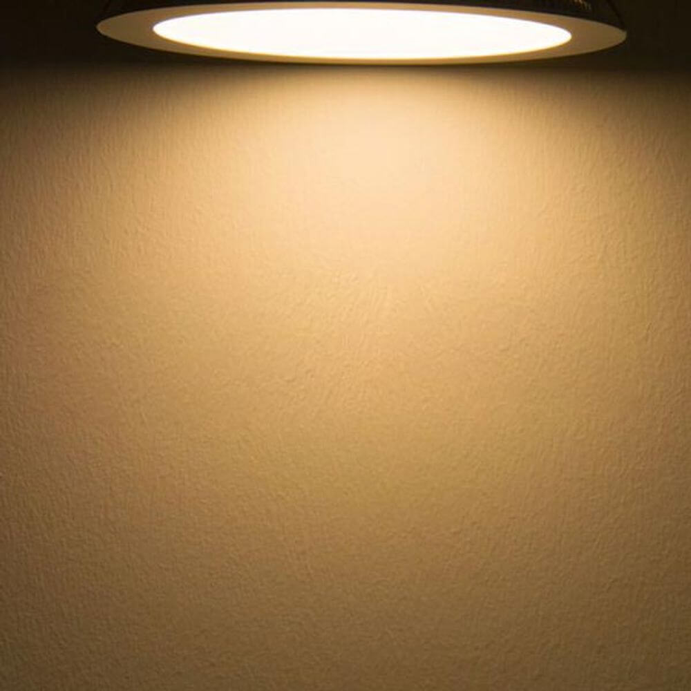 LED Einbaupanel Ø 22,5cm flach rund silber 18W Warmweiß strahlt warmes Licht auf eine Wand.