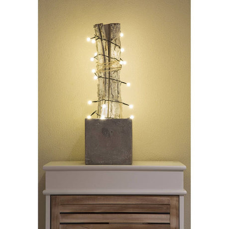LED Globelichterkette 50 runde Dioden Warmweiß batteriebetrieben dekoriert einen Holzstamm in Betonvase.