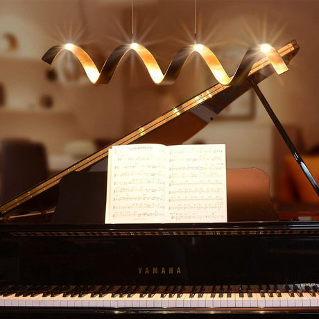 LED Lampe suspendue Helix couleur or, noire, placée au-dessus d’un piano, crée une ambiance élégante.