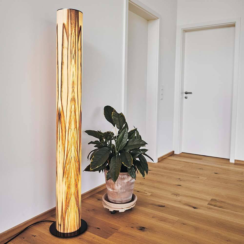 LED Holz-Stehleuchte Lucerna 160cm Satin Nussbaum in modernem Wohnraum mit Pflanze.