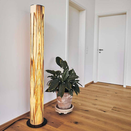LED trestativlampe i tre Lucerna 160 cm Satin valnøtt i et moderne oppholdsrom med plante.