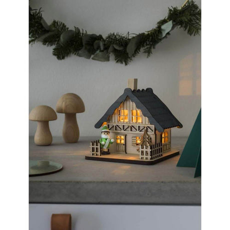 LED Holzsilhouette naturfarben Holzhaus mit grauem Dach 2 warmweiße Dioden batteriebetrieben Innen auf Tisch mit Dekoration.
