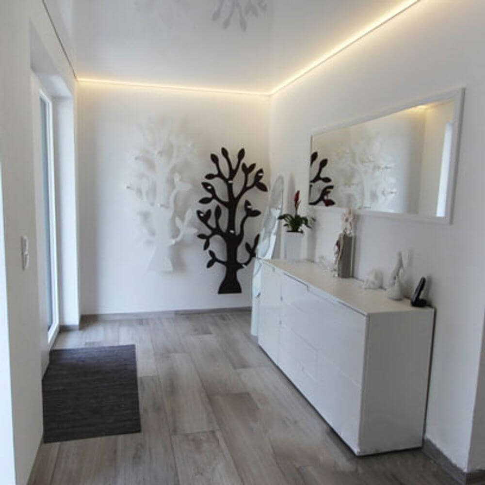 Moderne Diele mit LED-Lichtdecke, weißem Möbel und dekorativem Baumrelief an der Wand.