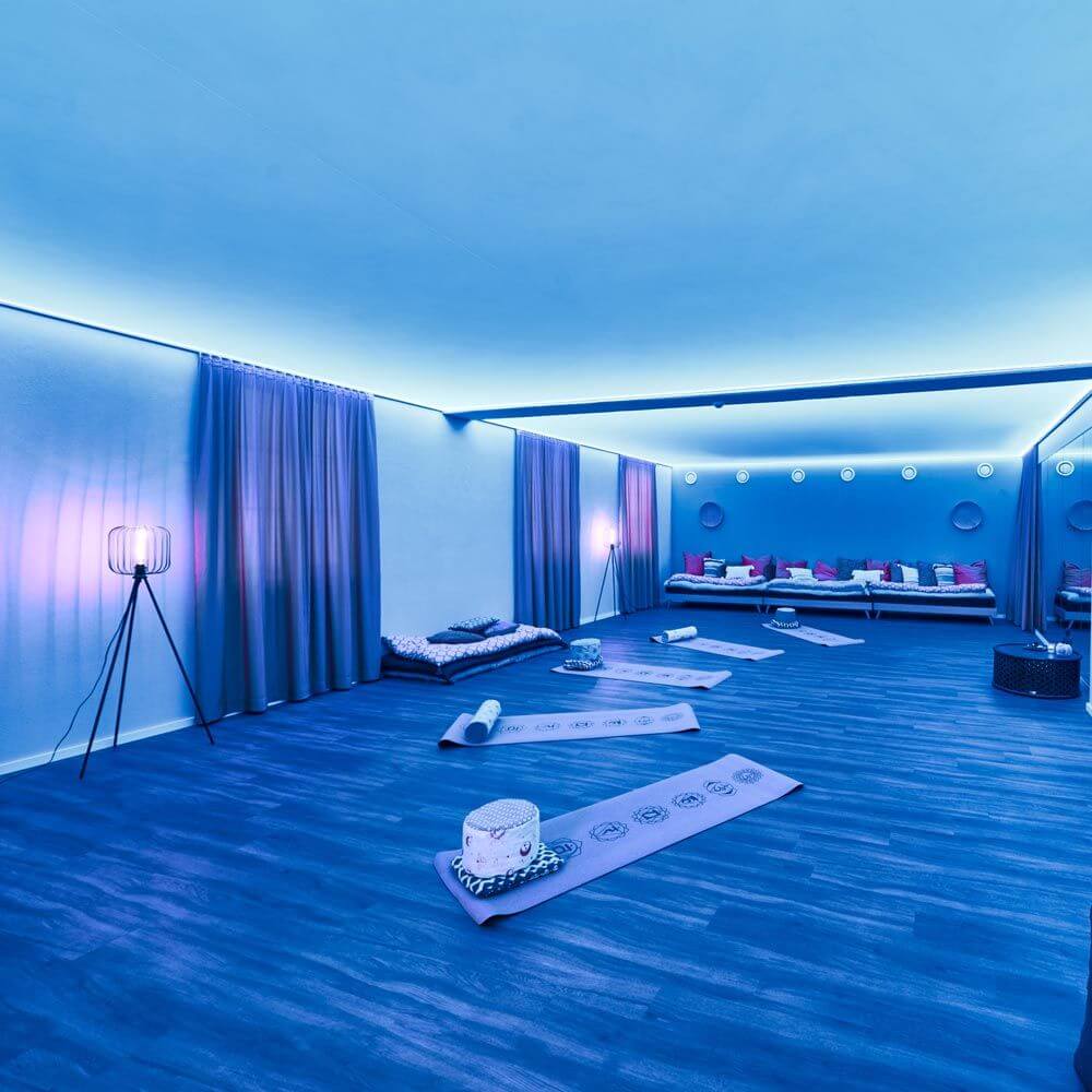 Moderne Raumbeleuchtung mit LED-Lichtdecke in blauen Farbtönen und Yoga-Matten zum Entspannen.