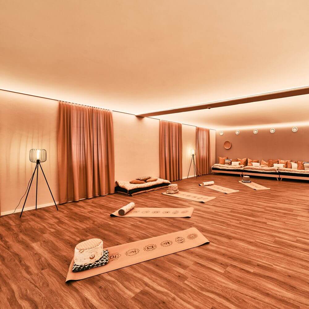 Gemütlicher Raum mit LED-Lichtdecke, Holzfußboden und gemütlichen Matten für Yoga- oder Entspannungseinheiten.