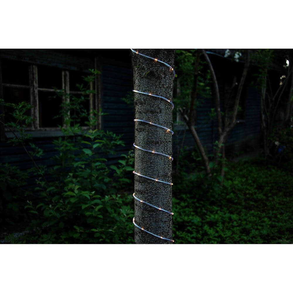 LED Mini Lichterschlauch 10m mit Lichtsensor Timer 130 Warmweiße Dioden batteriebetrieben IP44 um einen Baum gewickelt.