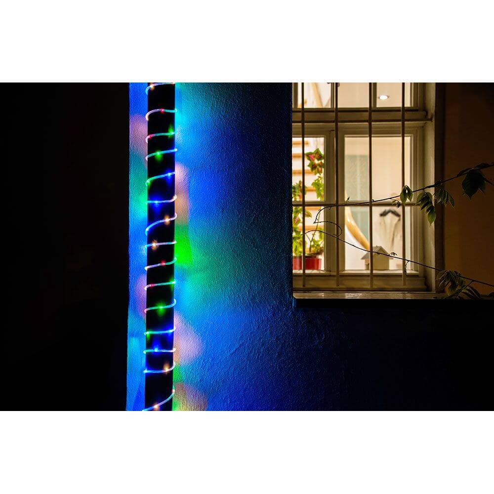 LED Mini Lichterschlauch 10m mit Lichtsensor Timer 130 bunte Dioden batteriebetrieben IP44 an einer Wand mit Fenster.